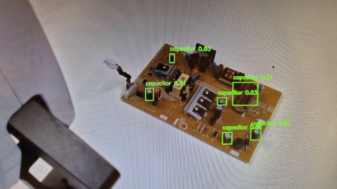 The trained YOLOv11 model detecting capacitors on a circuit board, with confidence scores shown live on screen.